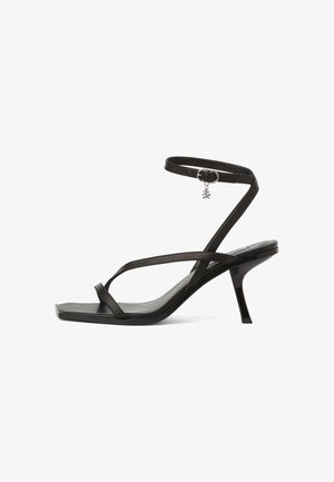 Črne sandale z naramnico, tanke naramnice okoli gležnja, koničastim nosom in majhno stilettto peto. Vključujejo srebrno čarobnico na naramnici okoli gležnja.