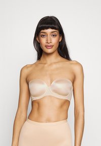Beige stroppeløs BH med glatt, blankt stoff, med undertrøye støtte, formede kopper og sømløst design, egnet for å bruke under ulike antrekk.