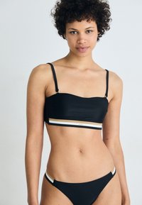 Set di bikini nero composto da un top corto con spalline sottili e una fascia a righe in oro e bianco. Tessuto liscio, design minimale, forma aderente.