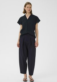 Top nero a maniche corte con scollo a V, abbinato a pantaloni blu navy dalla vestibilità ampia con pieghe frontali e silhouette rilassata.