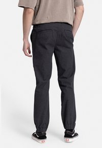 Sort joggingbukser med ribbede manchetter, elastisk talje og to baglommer, parret med en grå T-shirt med korte ærmer og sorte sneakers.