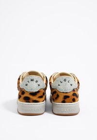 Tenis leopard print dengan aksen kulit putih yang tekstur dan retak di bagian tumit, tali sepatu beige, dan sol karet abu-abu.