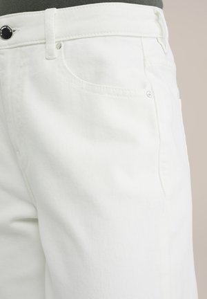 Baltas džinsus ar struktūru, priekšējām kabatām un pogu aizdari, tuvplāna skats, akcentējot auduma detaļas.