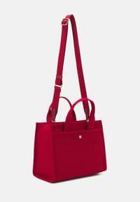 Sac cabas rectangulaire rouge avec doubles poignées et une longue bandoulière réglable, avec une poche avant à fermeture bouton.