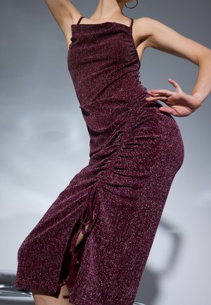 Bordeauxrotes, knielanges Kleid aus glänzendem, strukturiertem Stoff. Mit seitlichen Raffungen, dünnen Trägern und einem seitlichen Schlitz.