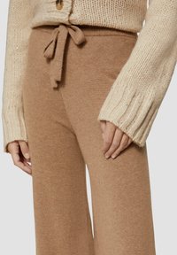 Lichtbruine gebreide broek met brede pijpen en een vastgebonden tailleband, gecombineerd met een crème gek textured trui met geribbelde mouwen en knoopdetail.