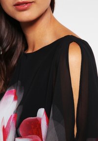 Schwarzes Kleid mit transparenten Ärmeln, das ein florales Muster in Rosa und Weiß aufweist, mit offenen Schultern und glatter Textur.