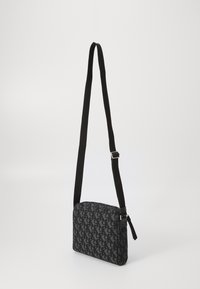 Black textile crossbody bag with a logo pattern, rectangular shape, adjustable strap, and zip closure. Smooth texture with subtle detailing.