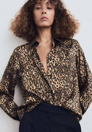 Blusa de estampado de leopardo en tejido sedoso, con un frente de botones, un corte relajado y mangas enrolladas. Pantalones negros completan el conjunto.