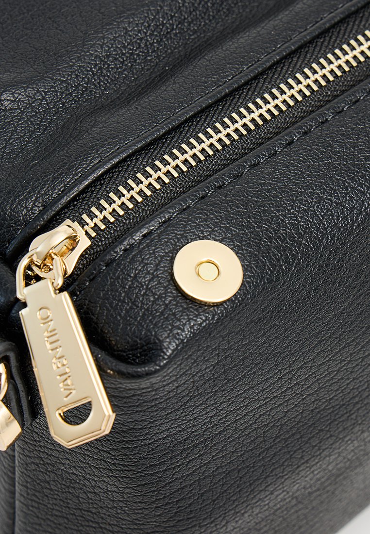 Coin de sac en cuir noir à texture grainée, mettant en avant une fermeture éclair et des accents en métal doré ; tirette de fermeture éclair avec gravure "Valentino" ; texture lisse.