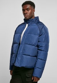 Navy blue puffer jacket with a quilted design, high collar, and snap-button closure. Smooth texture with a slightly glossy finish.