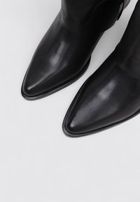 Botas de cuero negras de tacón puntiagudo y corte por el tobillo, con textura suave, costuras mínimas y una silueta elegante. Adecuadas para diversas ocasiones.