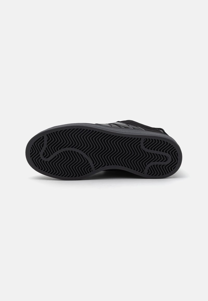 Suela de zapato deportivo negra con un patrón de banda de rodadura en zigzag. El material parece ser de goma; el diseño incluye bordes lisos y líneas curvas.