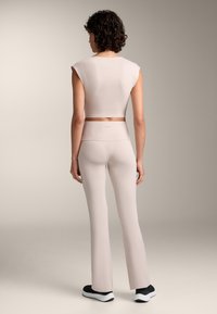 Svijetlo ružičasti kratki top s rukavima na kapicu uparen s svijetlo ružičastim lepršavim tajicama. Tkanina izgleda glatko; obuća ima crno-bijeli dizajn.