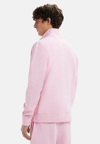 Sweatshirt rose avec un col montant, des manches longues et des poignets côtelés. Tissu doux et texturé avec une coupe décontractée et sans logos visibles.