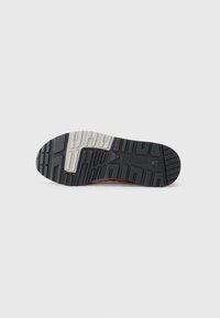 Zwarte en grijze rubberen sneakerzool met een gestructureerd loopvlak, voorzien van een centrale witte streep en branding aan de onderkant.