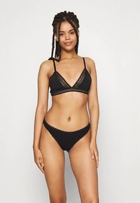 Black lingerie set featuring a triangular bralette and matching thong. The bralette has lace trim and adjustable straps, soft fabric.
