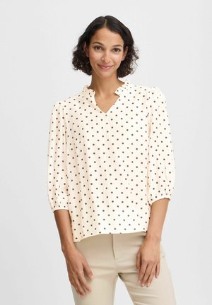 Blusa crema con pois marroni, scollatura a V e maniche puff a tre quarti. Tessuto morbido con una finitura testurizzata, vestibilità rilassata.