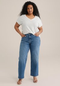 Maglietta a righe con maniche corte e scollatura a V, bianca e dorata, abbinata a jeans in denim blu a vita alta. Tessuto morbido, vestibilità rilassata, stile casual.