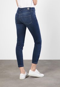 Dunkelblaue Jeans aus Denim mit einer taillierten Passform, die mit einem Reißverschluss-Detail am Knöchel und zwei Gesäßtaschen ausgestattet sind; kombiniert mit weißen Sneakers.