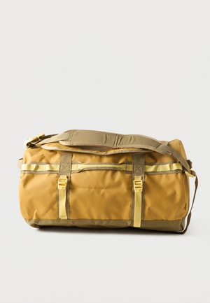 Bolsa de viaje grande en color marrón claro y amarillo con correa ajustable para el hombro y cierres laterales de hebilla sobre un fondo claro liso.