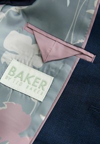 Marineblazer mit einem Blütenmusterfutter in gedämpften Farben; verfügt über eine pinkfarbene Akzenttasche und ein gewebtes Etikett mit der Aufschrift "BAKER by TED BAKER".