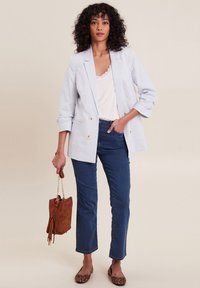 Blazer a righe in tessuto azzurro chiaro con doppi bottoni, abbinato a una maglietta bianca e jeans blu. Borsa in suede marrone con frange; ballerine a stampa animale.