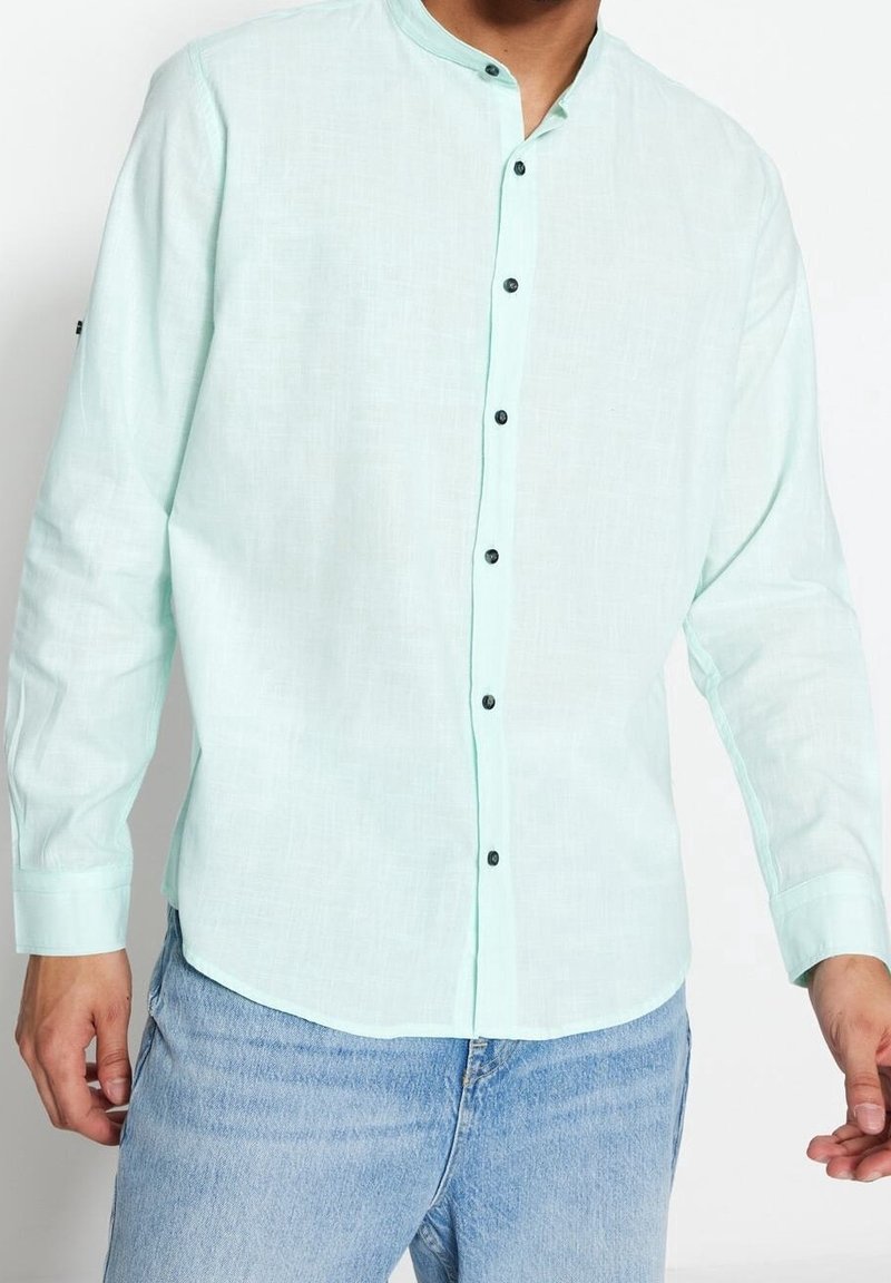 Camicia a maniche lunghe verde menta chiaro con colletto rotondo, bottoni neri e un tessuto strutturato. Finitura liscia e orlo curvato.
