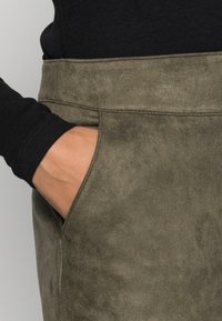 Olivengrøn nederdel i imiteret ruskind med glat tekstur og sidelomme, kombineret med en sort ribbet langærmet top.