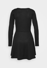 Robe noire côtelée à manches longues, taille cintrée et jupe légèrement évasée, vue de dos sur un fond uni.