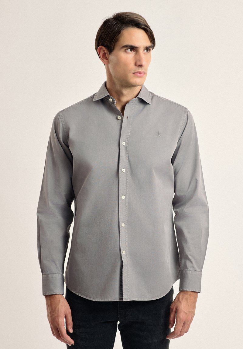 Camisa gris de botones con cuello, mangas largas y un pequeño logo bordado en el pecho; presenta una tela suave y texturizada.