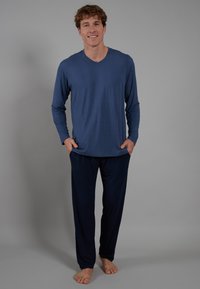 Langermige V-hals shirt van zachtblauwe stof, gecombineerd met donkere marineblauwe broek. Beide kledingstukken hebben een ontspannen pasvorm en een gladde textuur.