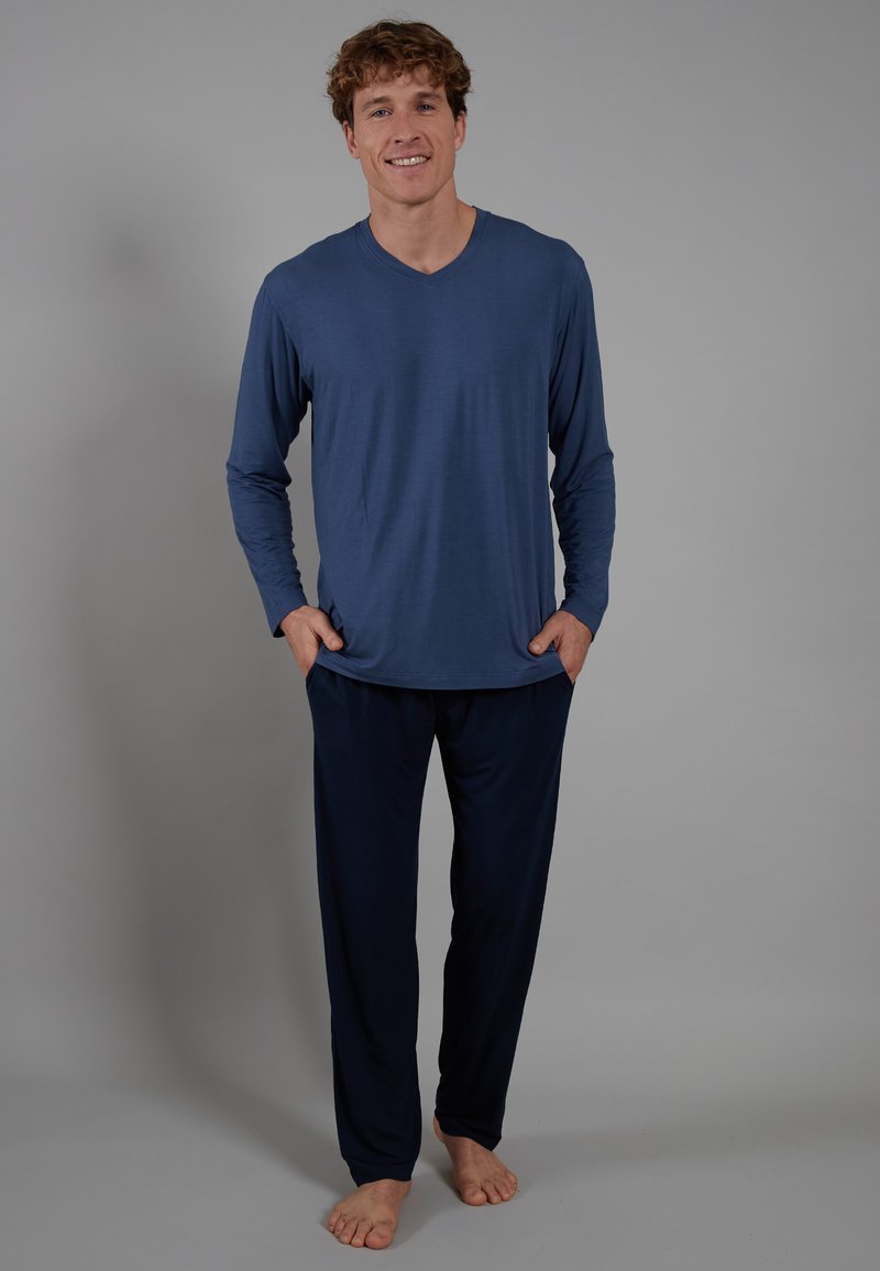 Langermige V-hals shirt van zachtblauwe stof, gecombineerd met donkere marineblauwe broek. Beide kledingstukken hebben een ontspannen pasvorm en een gladde textuur.