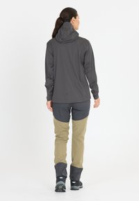 Grå vattentät jacka med en åtsittande huva, tillsammans med beige byxor med grå detaljer och tryckknappar vid mudden. Svarta vandringsskor.