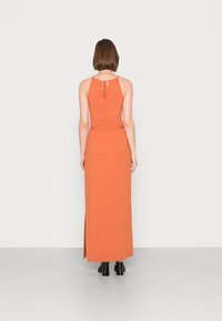 Vestido maxi na cor ferrugem com cintura ajustada, decote halter e fendas laterais. Feito de um tecido macio com um detalhe de laço nas costas.