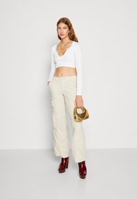 Hvit ripset cropped topp, beige cargo bukser med lommer, røde platåhæler og en gull metallisk håndveske. Lange ermer og V-hals design.