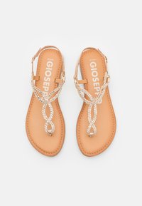 Las sandalias planas marrones cuentan con tiras trenzadas de color plata que crean un diseño en bucle, con una plantilla de cuero suave y hebillas ajustables. Logotipo de la marca en el interior.