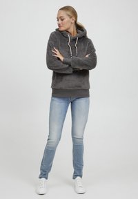 Hoodie grigio peloso con cordini, abbinato a jeans azzurri chiari e sneakers bianche. Il hoodie ha polsini e vita a coste.