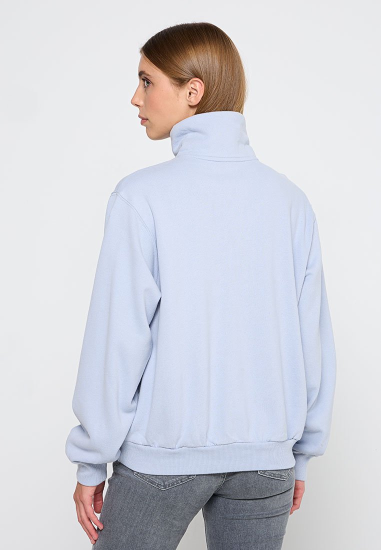 Helles blaues Fleece-Pullover mit hohem Kragen, gerippten Bündchen und Saum, der einen lockeren Schnitt und eine weiche Textur aufweist.