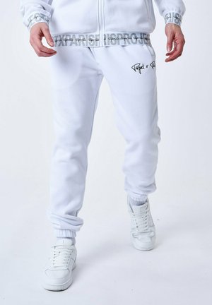 Pantalones de chándal blancos con puños elásticos, que presentan un logotipo texturizado en el muslo izquierdo y una cinturilla con un patrón que dice "PARIS PROJECT" en gris.