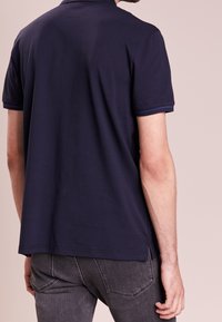 Tmavě modré polo tričko z bavlny s krátkými rukávy, s límečkem a kontrastním lemem podél rukávů. Jednoduchý, jednobarevný design.