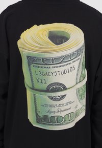 Sweat-shirt noir avec un grand graphisme représentant un rouleau de billets de cent dollars américains, affichant une impression très détaillée et des couleurs éclatantes.