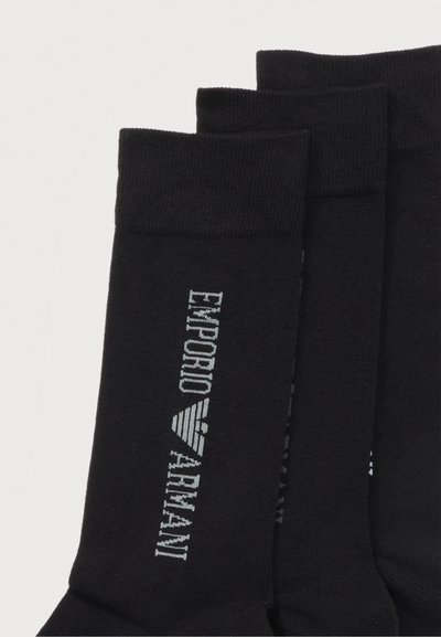 Τρία ζευγάρια μαύρες κάλτσες με λευκό κάθετο κείμενο «EMPORIO ARMANI» και λογότυπο στη πλευρά, διπλωμένες με εμφανείς τις μανσέτες.