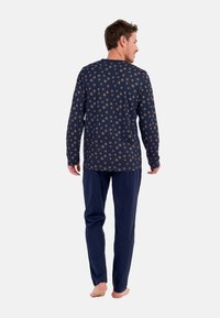 Laivastonsininen pyjama-asuste, jossa on pitkähihaiset paita, jossa on pieniä geometrisia kuvioita, ja yksiväriset housut. Pehmeä kangas ja rento malli.