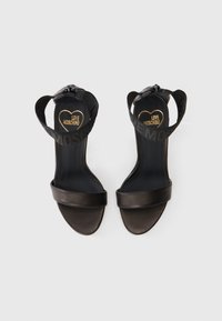 Μαύρες ψηλοτάκουνες σαγιονάρες με δυο φαρδείς ιμάντες και υφασμάτινο ιμάντα στον αστράγαλο, που διαθέτουν λογότυπο σε χρυσό στη σόλα. Λείο δέρμα.