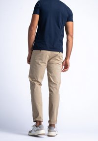 Tmavě modré přiléhavé tričko, khaki chinos kalhoty a šedé tenisky s bílými podrážkami; chinos kalhoty mají vyhrnuté lemy, minimální hardwarové detaily.