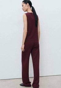 Bordeaux mouwloze top met een relaxed fit, gecombineerd met bijpassende wijde broekspijpen. Glad, textuurstof zonder patronen of versieringen.