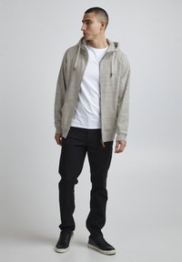 Hanorac zip-up gri deschis cu șnururi, purtat cu un tricou alb, blugi negri și adidași negri, având un croi casual și țesătură texturată.