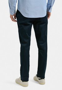 Mörk marinblå byxor i bomull, med rak passform och uppvikta benslut, kombinerade med ljusa sneakers och en skjorta med knappar.