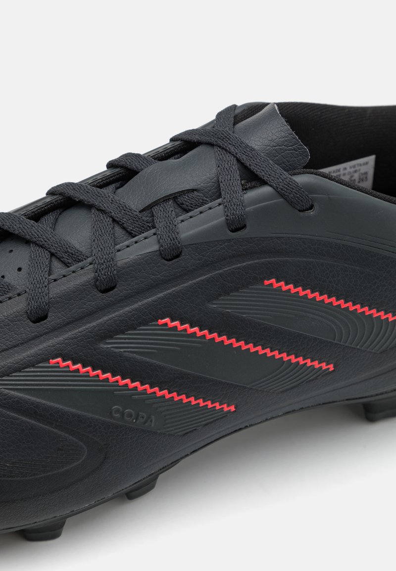 Botín de fútbol negro con piel texturizada, un diseño aerodinámico, tres rayas rojas en zigzag y cordones negros.